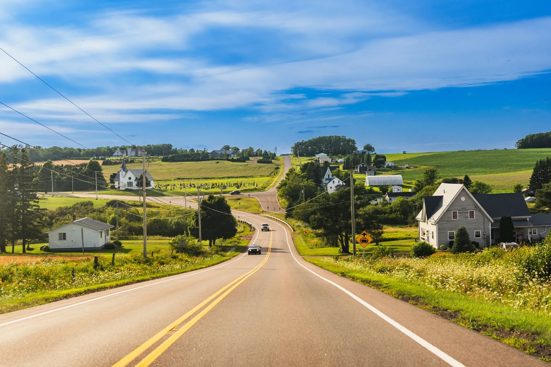 A quiet country road lined with farmhouses and open fields.